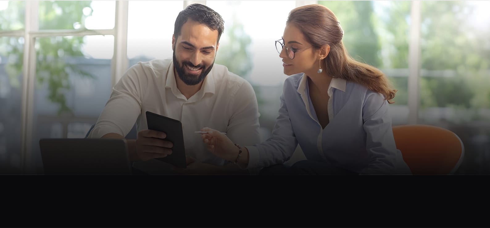 Two professionals collaborating, with the man smiling while reviewing a partnership agreement on a device and the partner attentively observing.